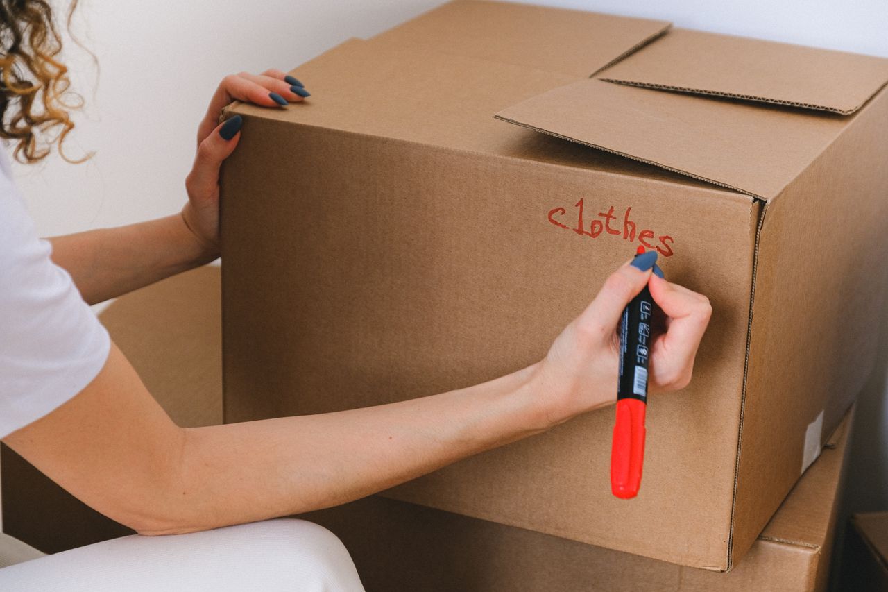 A close-up view of a woman indoors writing on a cardboard box with a red marker.